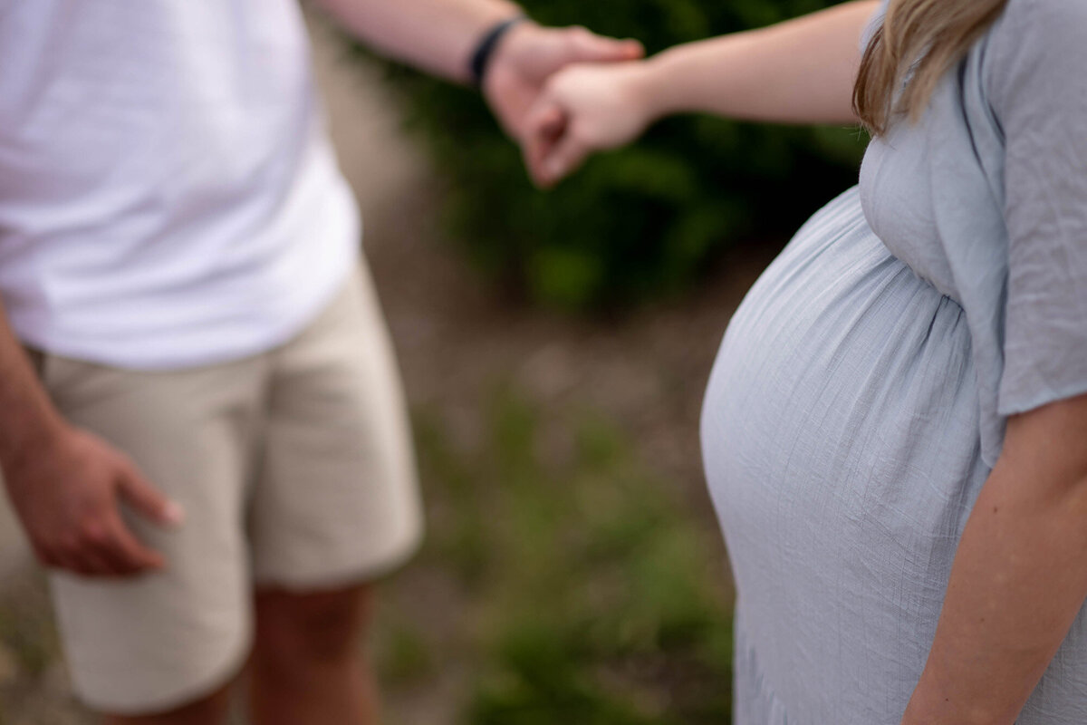 Pregnant couple holds hands in a park over the bump