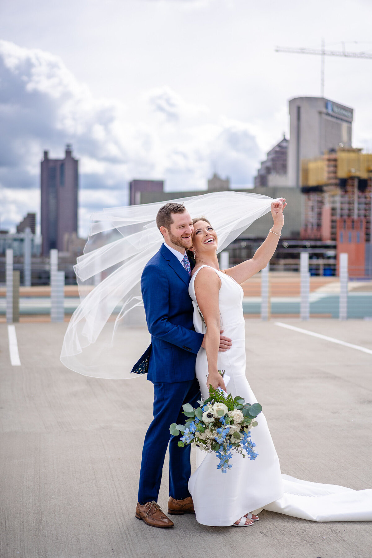 Bride, Vicky, swings her veil in the wind with her groom, David Hitch, on top of a parking garage with the Columbus skyline in the background.