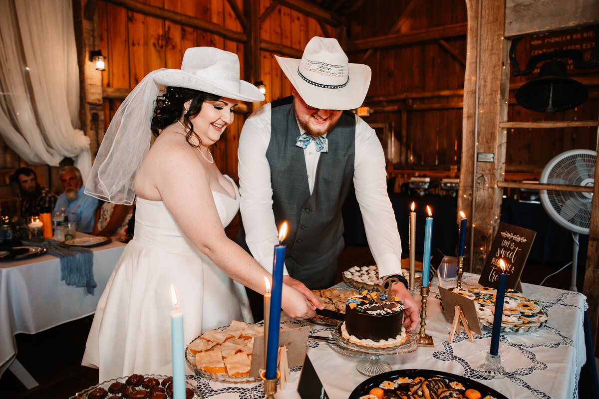 Newlyweds in Cowboy hats cut the cake at the desert table covered in options