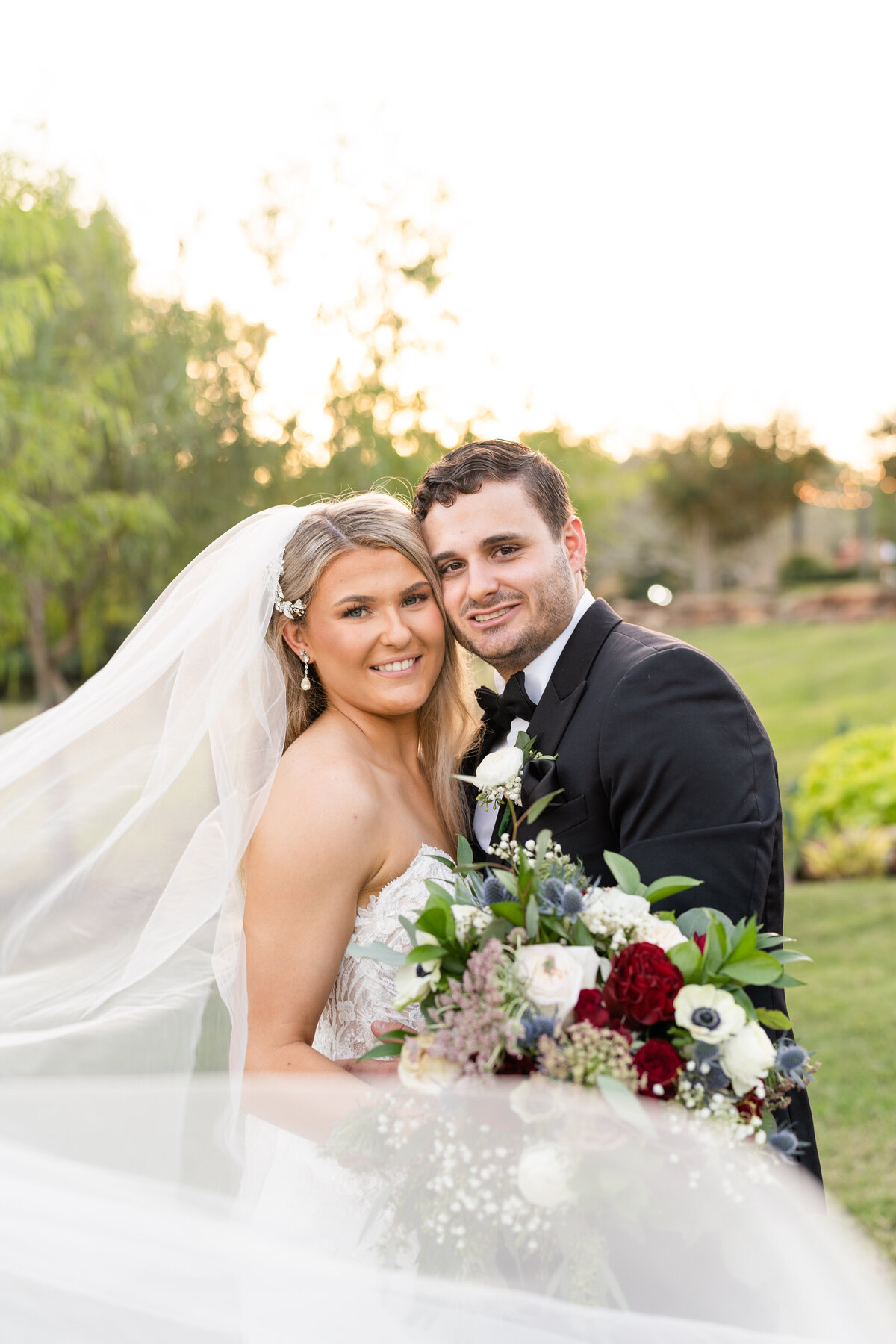 Bride and Groom hugging each other and smiling at camera with large bouquet and veil in front of camera after ceremony during couples sunset photos at the Springs Wallisville