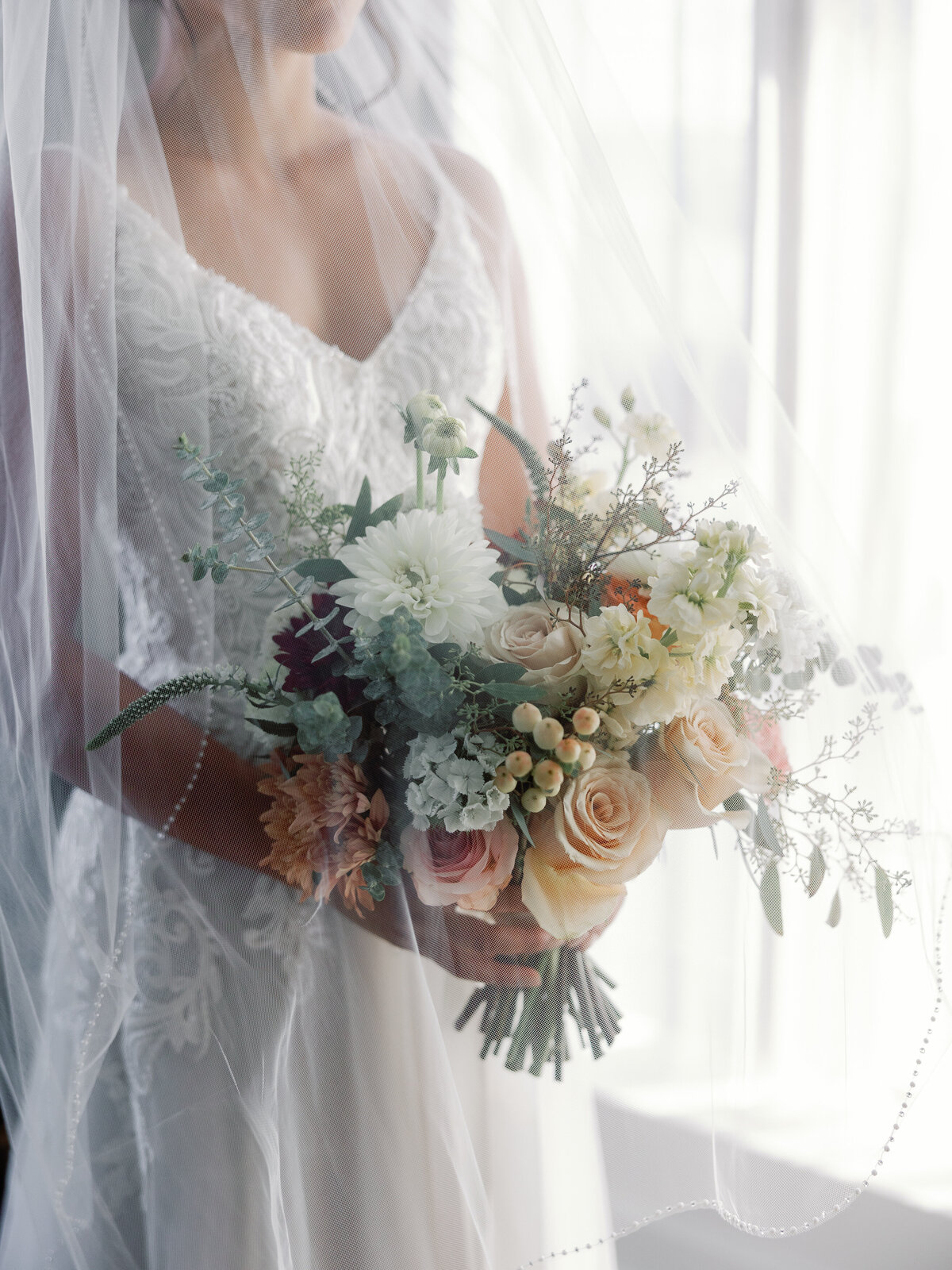 A bride holds her bouquet of summer flowers as her veil cascades over her body