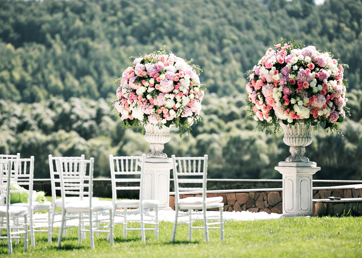 Beautiful wedding ceremony design decoration with fresh roses in stone urns outdoors for a luxury destination celebration.