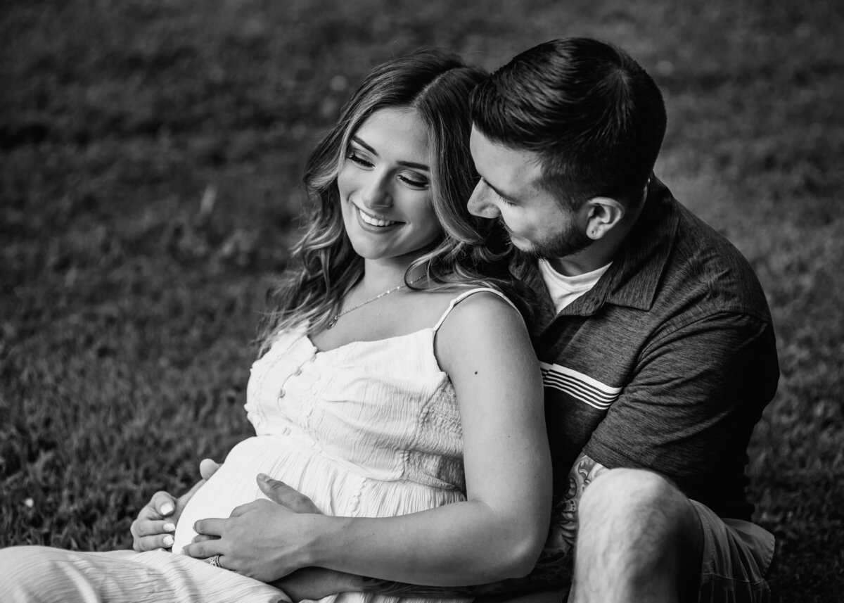Pittsburgh maternity photographer captures a loving, black and white photo of a pregnant couple embracing in the grass.
