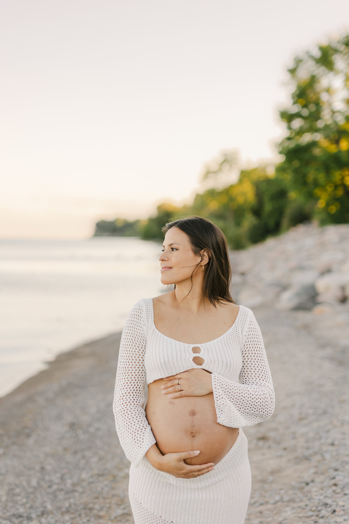 A mother to be looking at the water and holding her pregnant belly in a Toronto beach