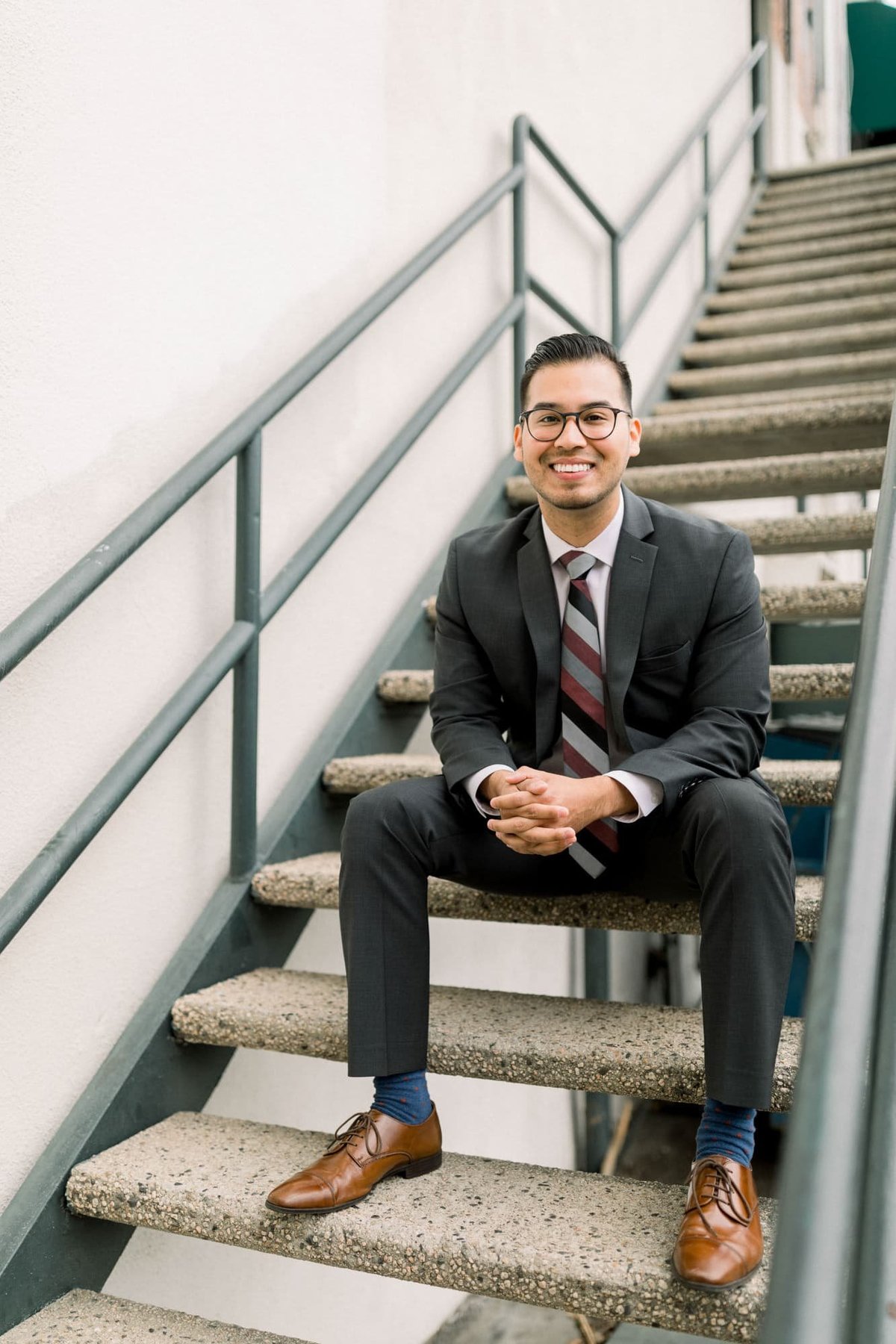 College senior poses in his suit while sitting on outdoor staircase