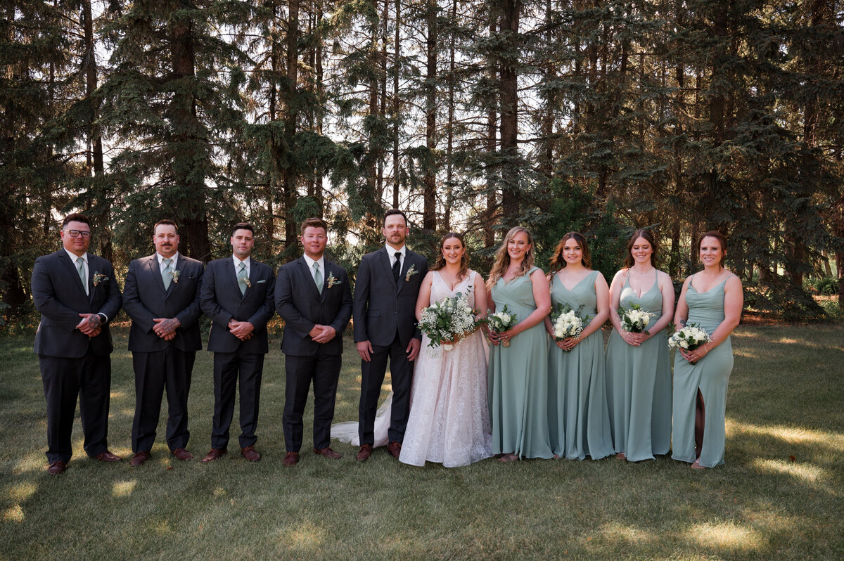 wedding party posing for portraits in a green field with trees in the background