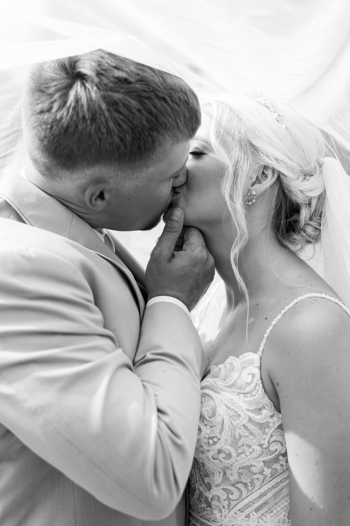 A black and white photo of a bride and groom sharing a kiss at their wedding at a Charlotte area vineyard.