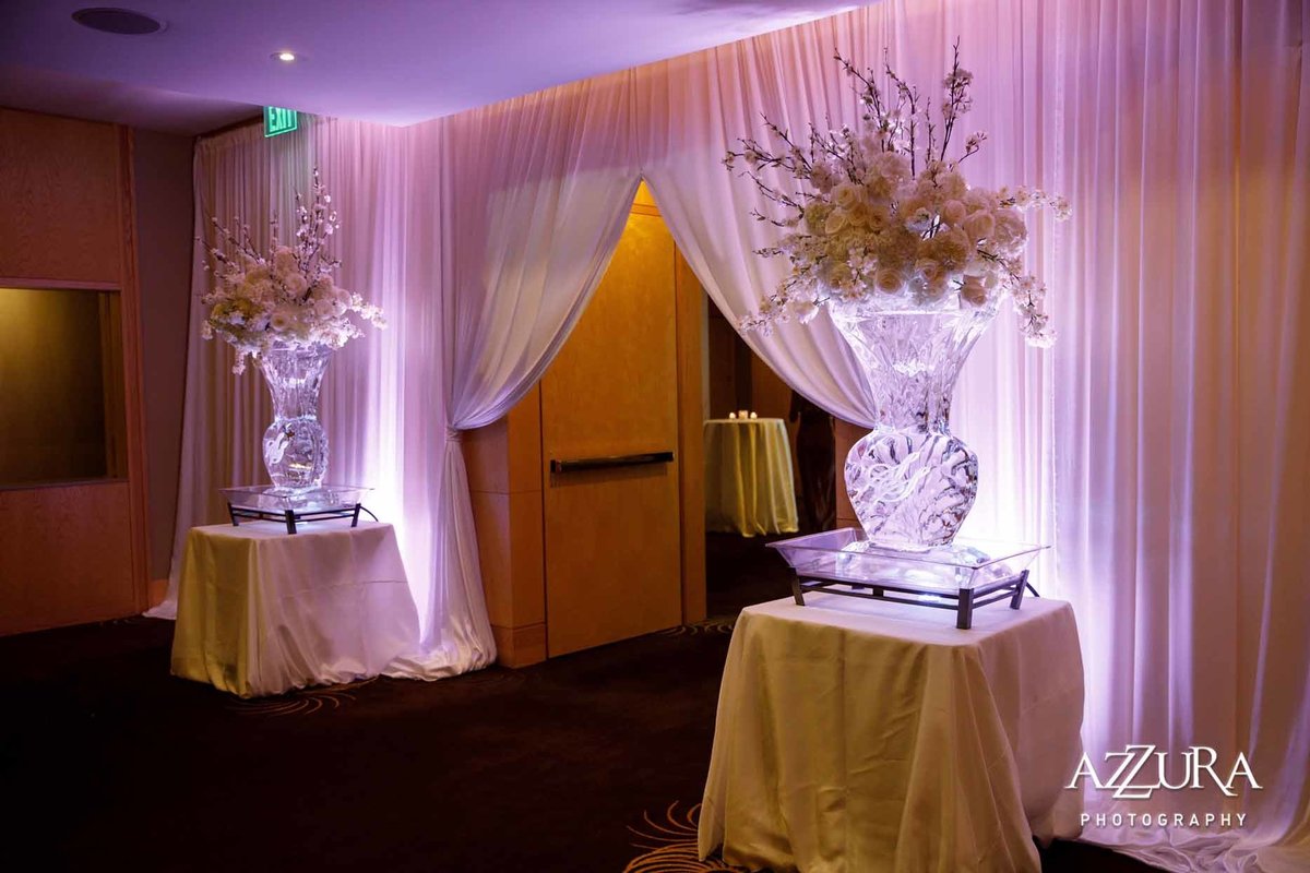 large floral arrangements in large ice vases at draped entrance to wedding