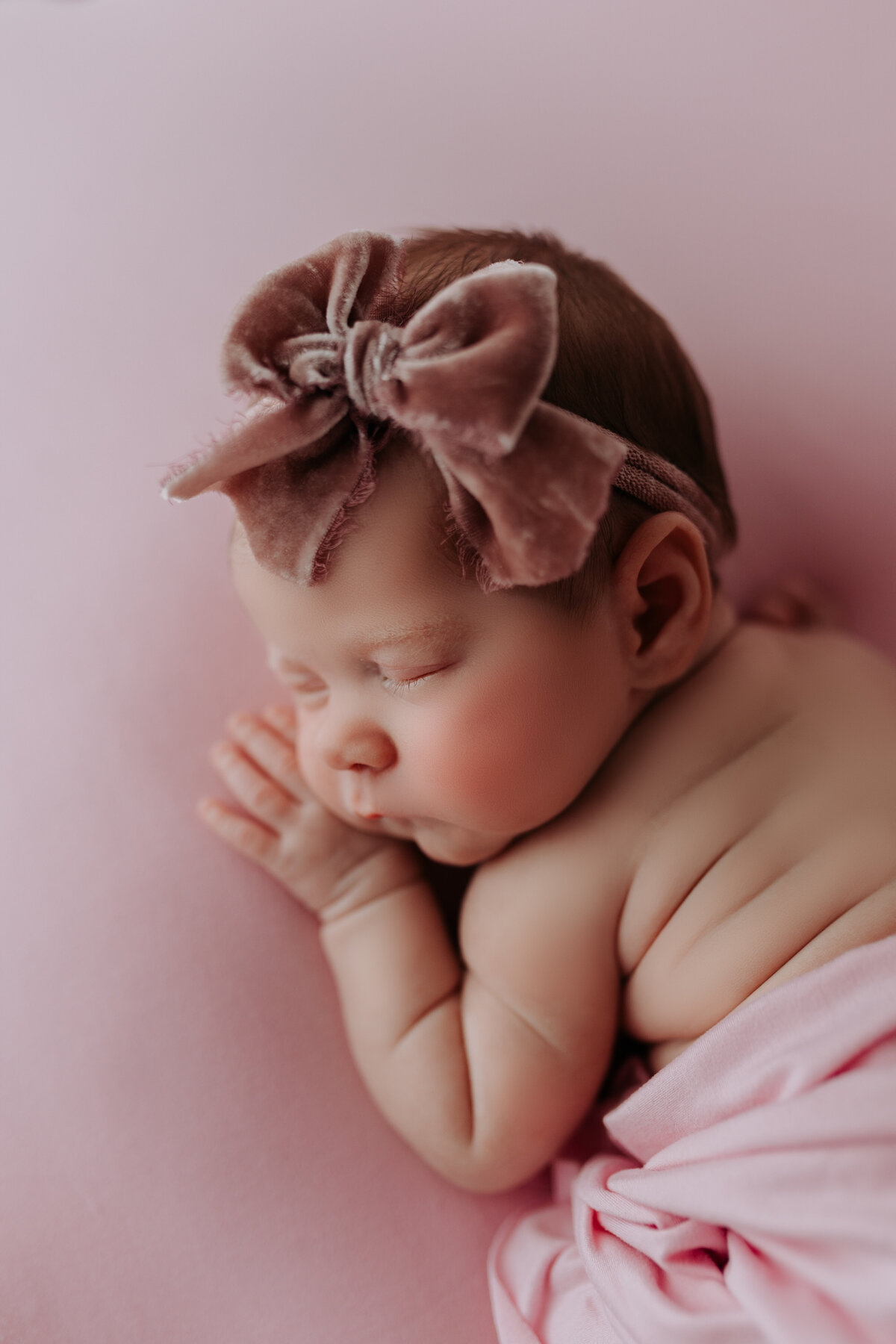 newborn girl wearing bow with pink backdrop in side laying pose
