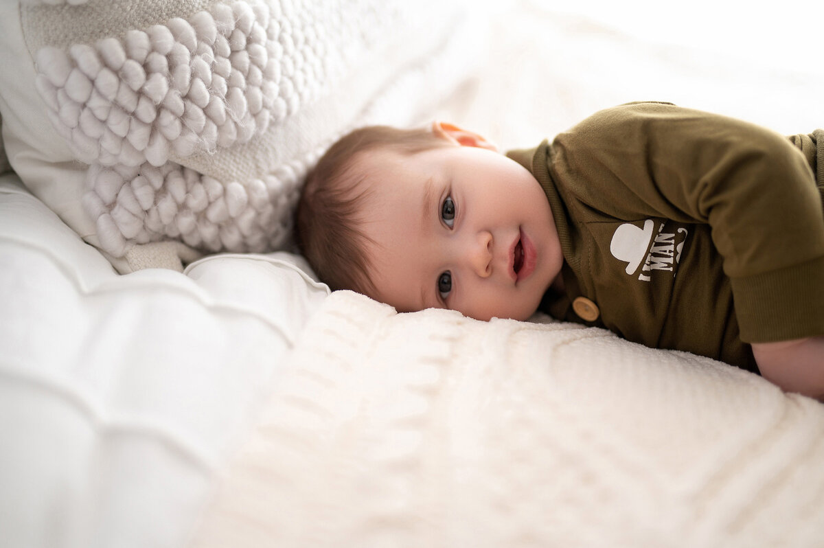 A baby boy snuggles into fluffy white bedding for his portrait in our Waukesha photo studio.