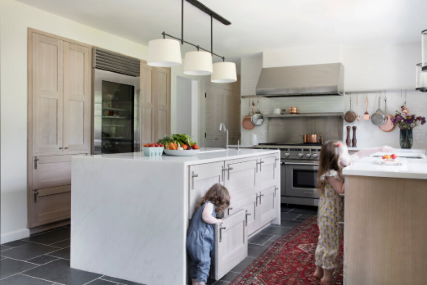 Interior designers in Westwood design a natural oak kitchen with slate flooring, vintage rugs, panel-ready appliances, stainless accents, and bronze lighting.