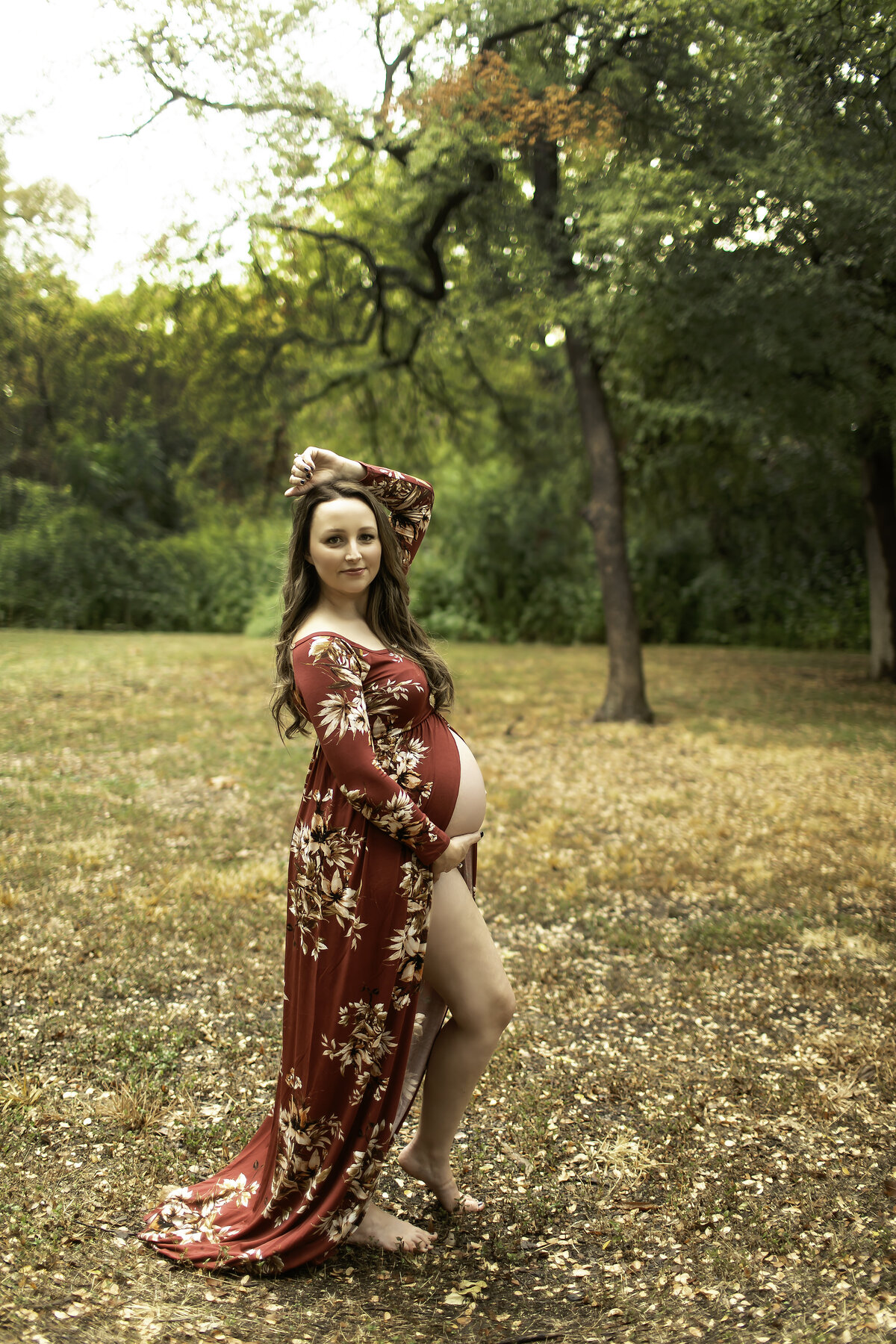 A vibrant maternity photo of the expectant mom in a red dress, standing confidently on a park path at Trinity Park, with sunlight filtering through the trees, captured by Chunky Monkey Photography.