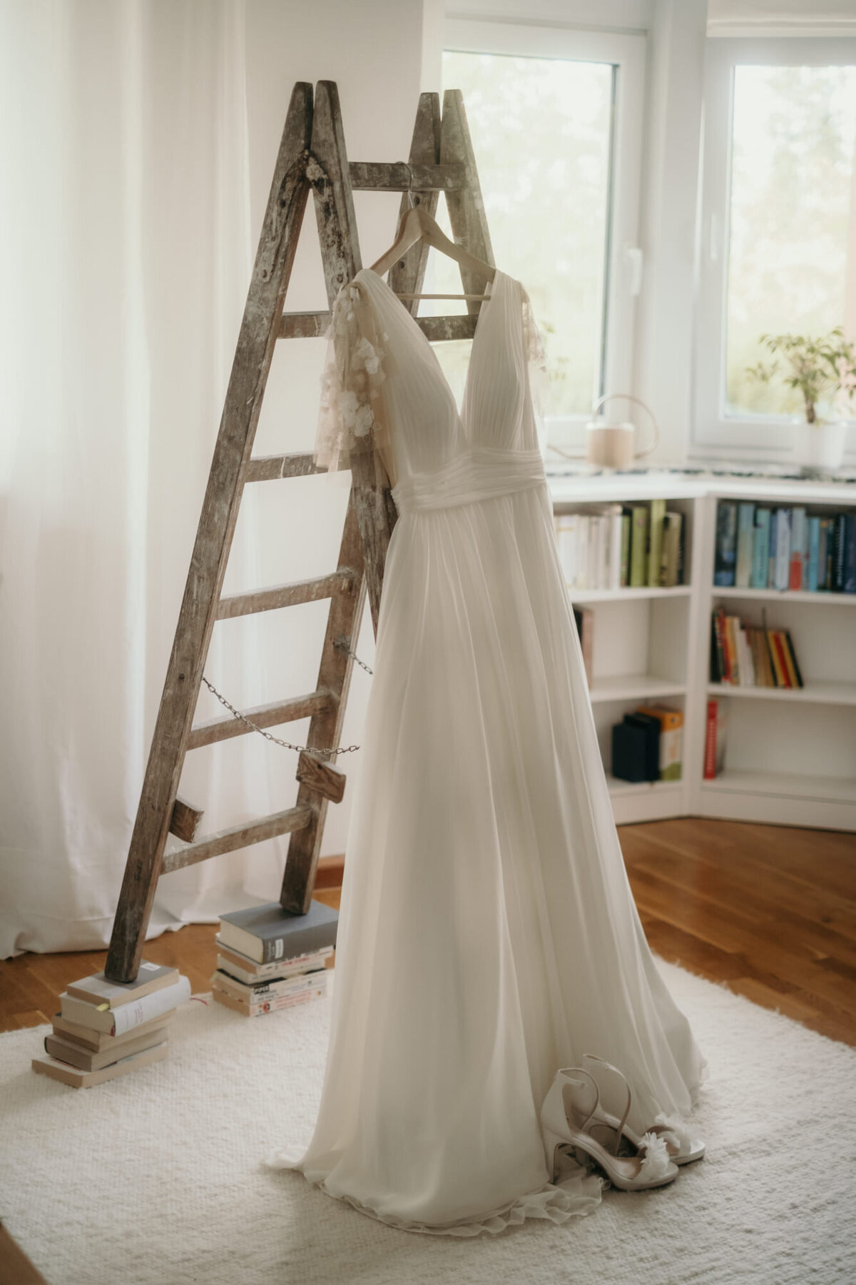 Das Brautkleid hängt an einer Holzleiter, deren Füße auf Büchern stehen.