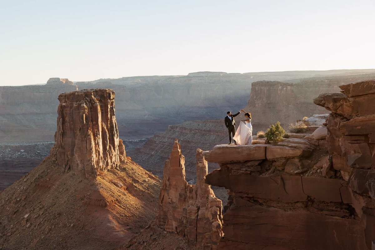 A groom twirls his bride as the sun sets during their Marlboro Point elopement in Moab. They are surrounded by an epic backdrop