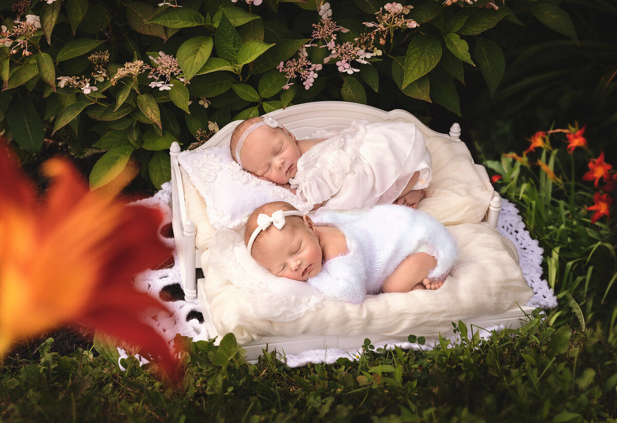 Greater Toronto Newborn photographer twins in white outdoors sleeping on a white trundle bed surrounded by flowers.