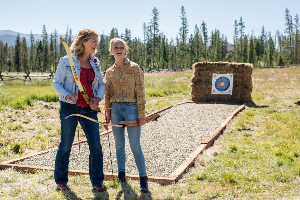 women standing in front of an archary target holding a bow and arrow chatting