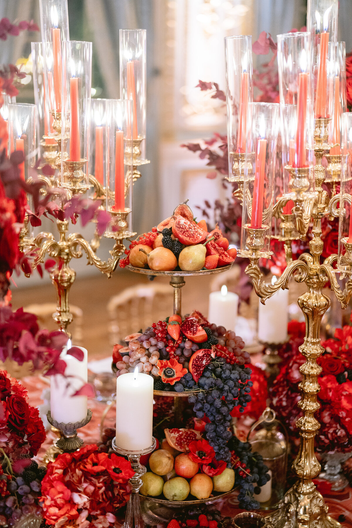 The photo was taken at the stunning Shangri La Hotel & Ritz Paris Hotel in Paris, France, by the talented photographer Matteo Coltro. Videography by Zen Film Works captures the luxurious table setting, showcasing gold candelabras holding red candles, set amidst a backdrop of rich autumnal flowers. The centerpiece steals the show with a bountiful three-tiered fruit display boasting pomegranates, figs, grapes, apples, and peaches, elegantly accompanied by white pillar candles.