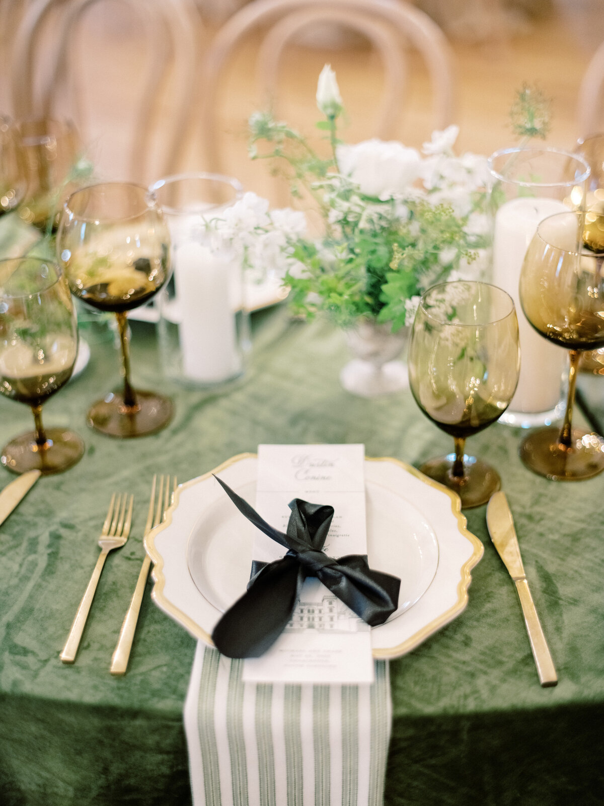 A detailed shot of a fine dining table set with elegant plates, black ribbon bows, and greenery, showcasing a stylish and sophisticated dining experience.