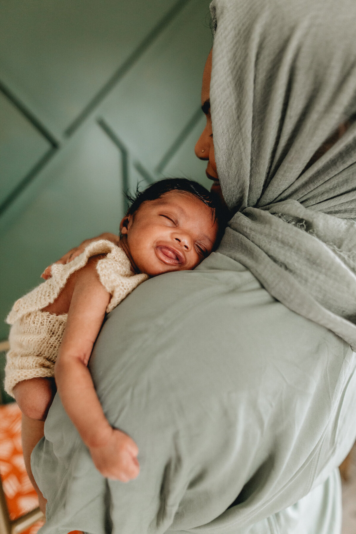 Newborn photo with a newborn snuggles and smiles on moms shoulder