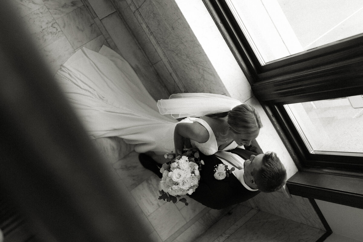 Bride and groom cozy up lovingly in the corner of a courthouse following their downtown Duluth elopement. 
