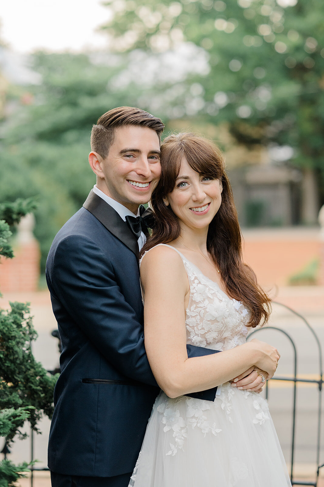 A bride wearing a white wedding dress and a groom wearing a tuxedo stand outside of Birkby House in Leesburg, Virginia