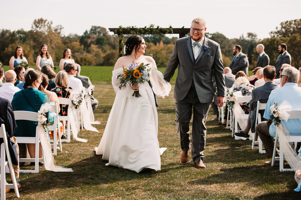 A happy bride smiles at her new husband while walking back up the aisle of their outdoor ceremony