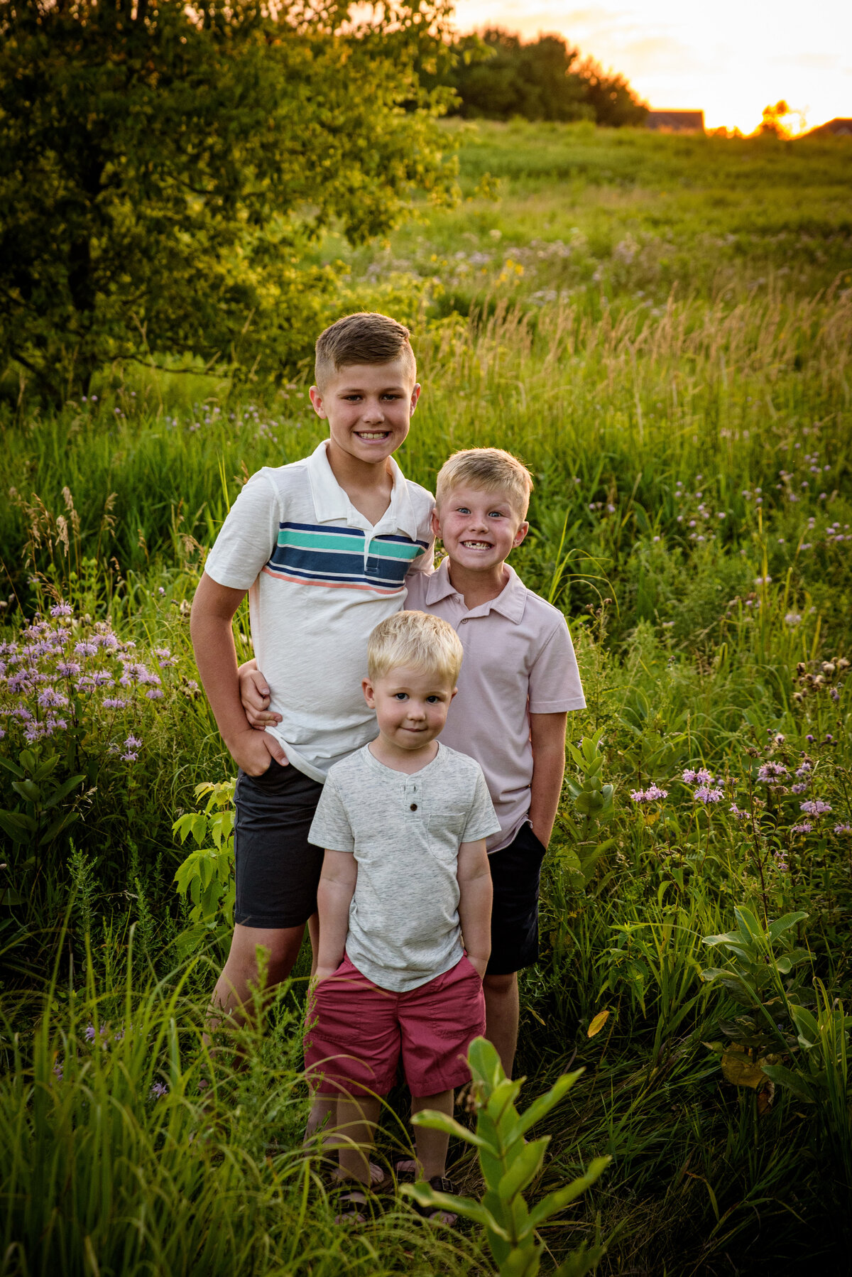 Sibling portrait of three boys standing in long grassy field with a beautiful sunset at Fonferek Glen County Park near Green Bay, Wisconsin