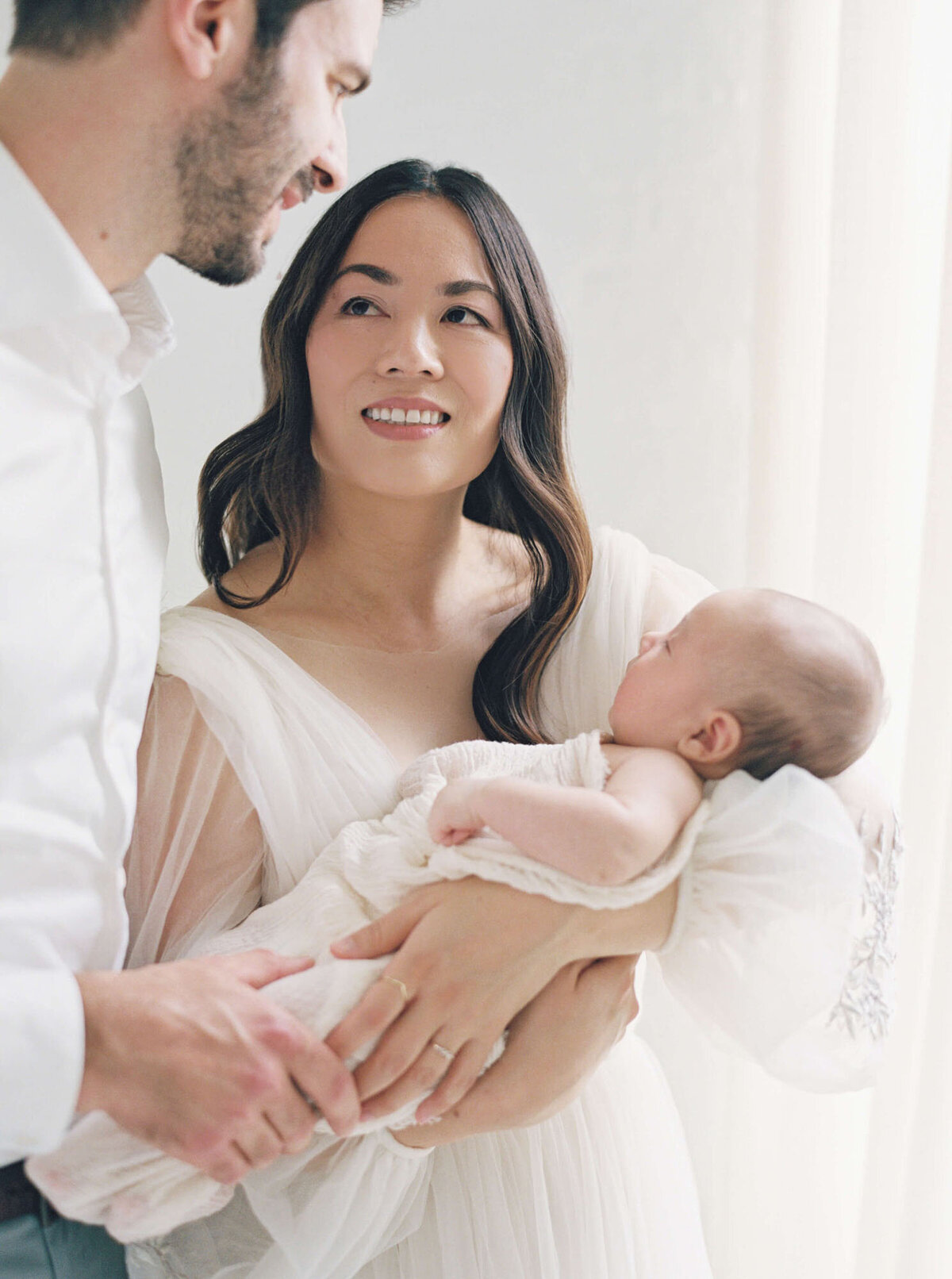 Parents smiling at each other while holding newborn, newborn photography Bay Area.