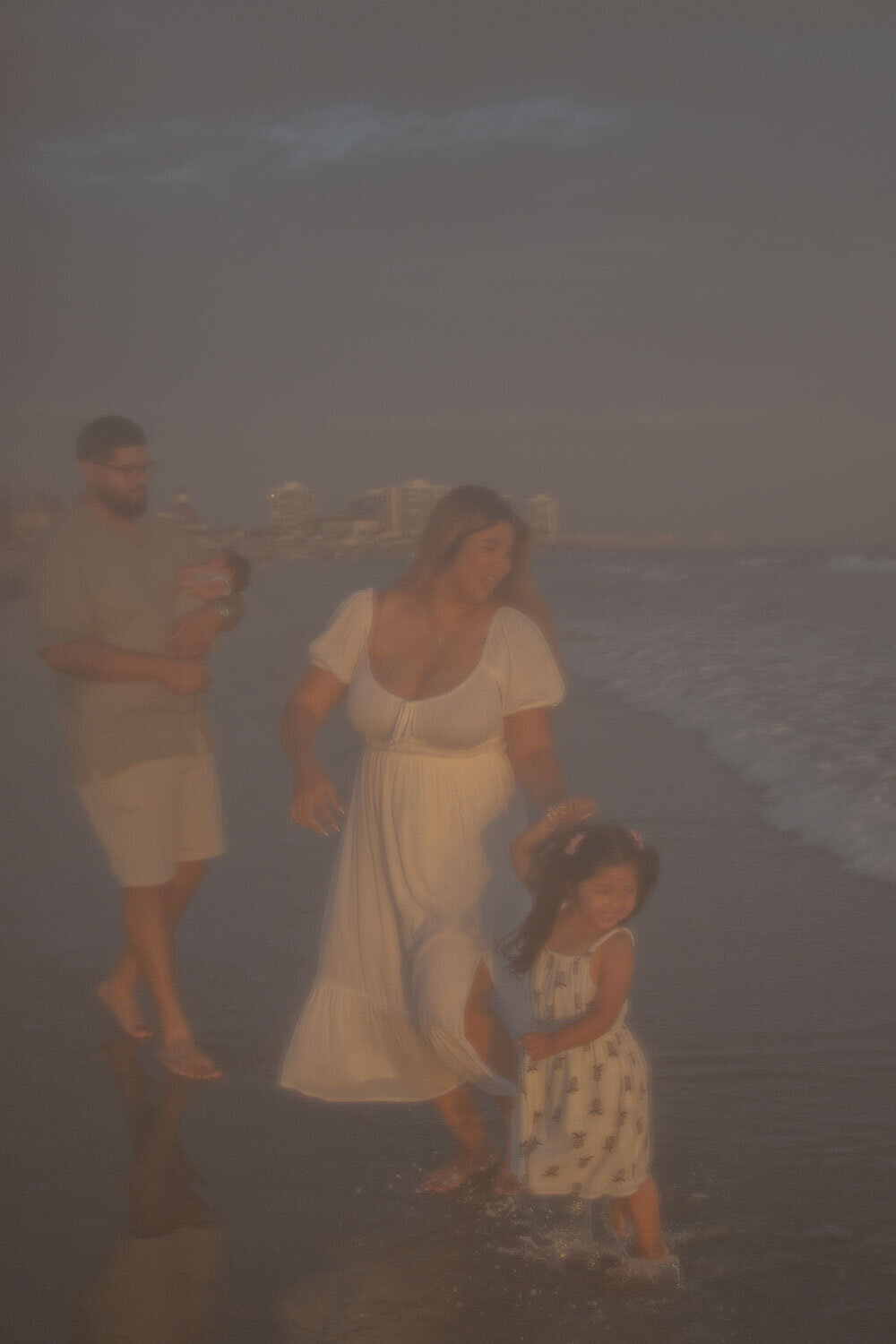 Family playing on the beach at sunset, capturing a candid moment.