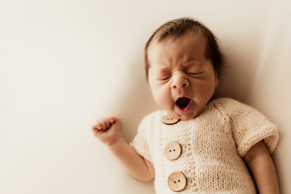 Baby boy wearing a cream romper yawns.