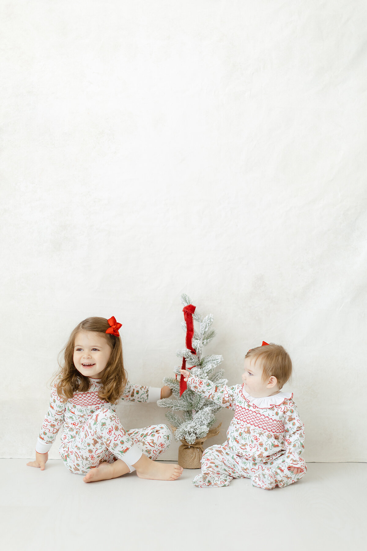 Two young children playing with a mini christmas tree and modeling christmas clothes for Dondolo
