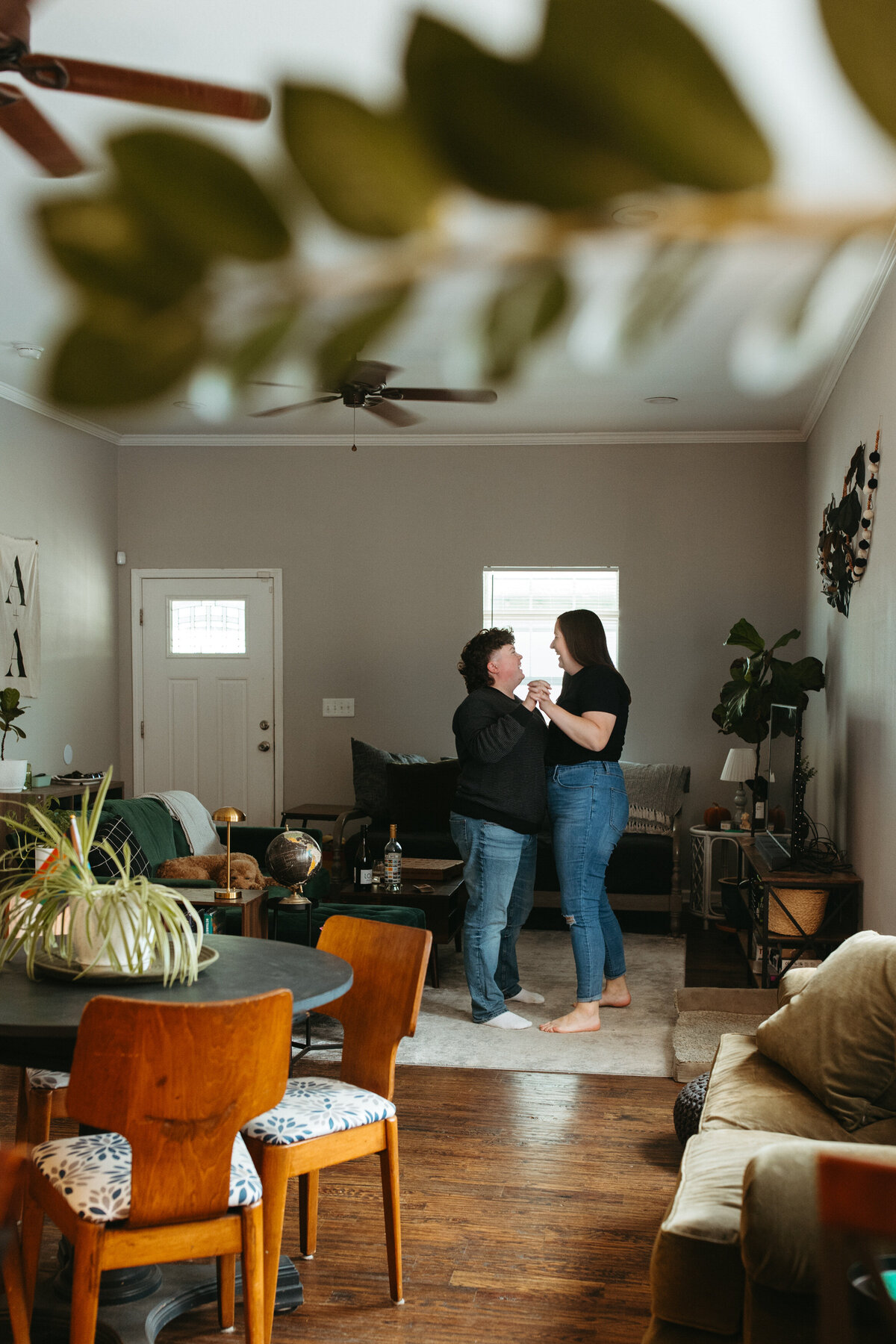 A candid shot from a living room perspective, capturing two individuals in a playful dance, surrounded by vibrant houseplants
