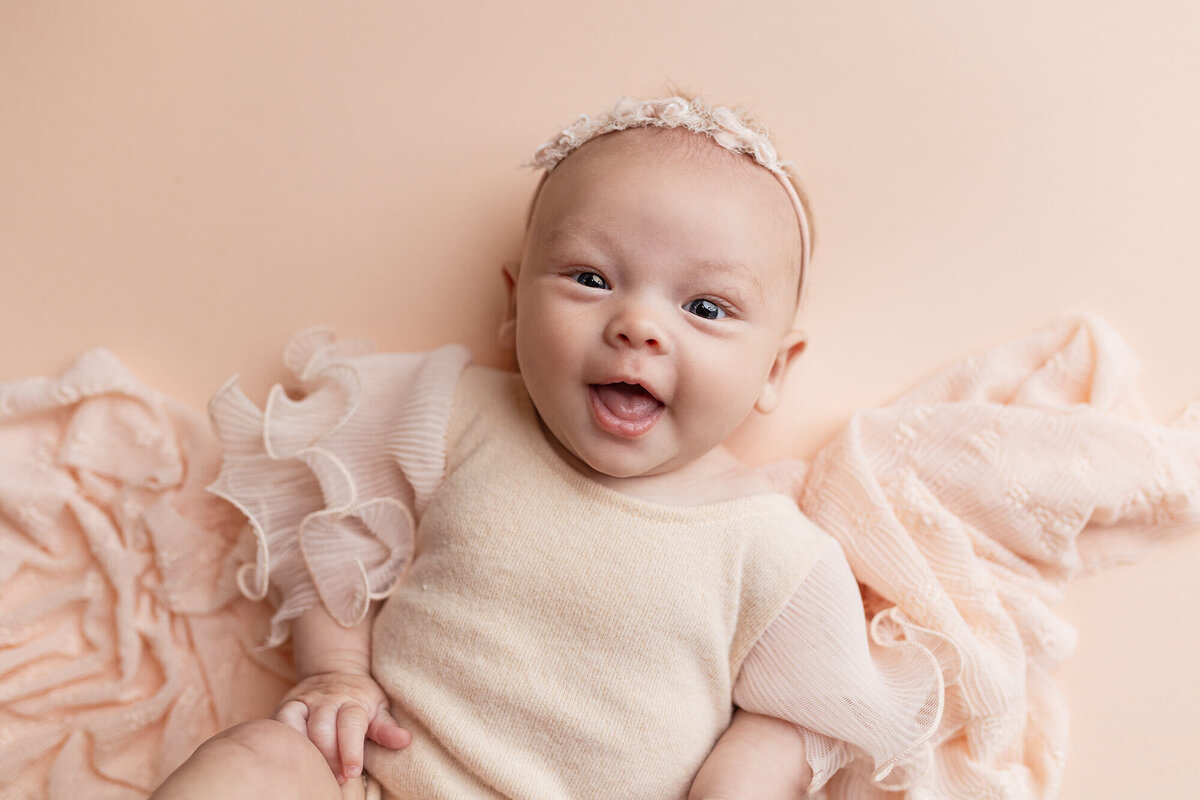 3-month old girl in pink smiles at the camera for her session in Minnesota.