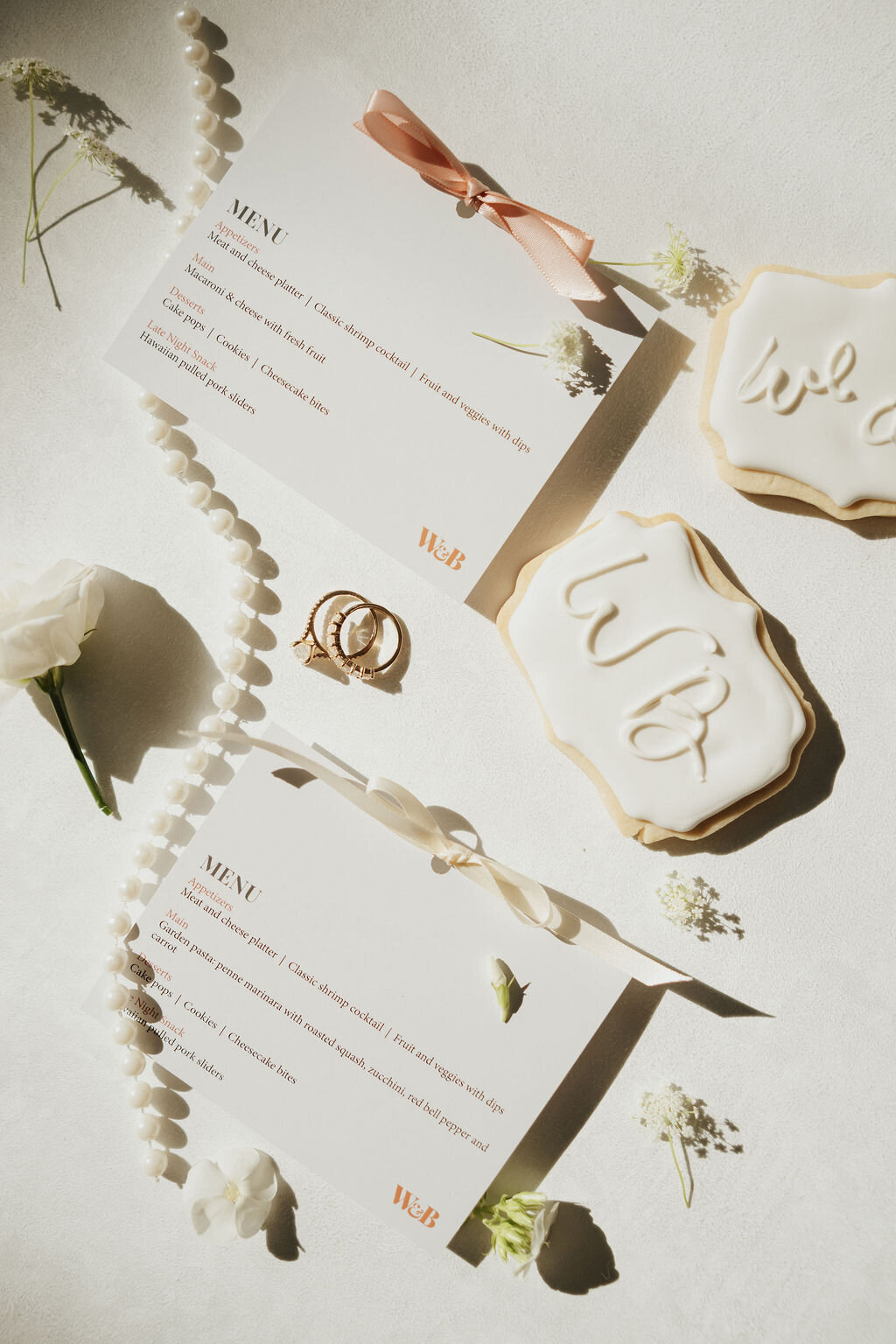 wedding menu escort cards flat lay with ribbon detail, wedding pearls and monogram cookies