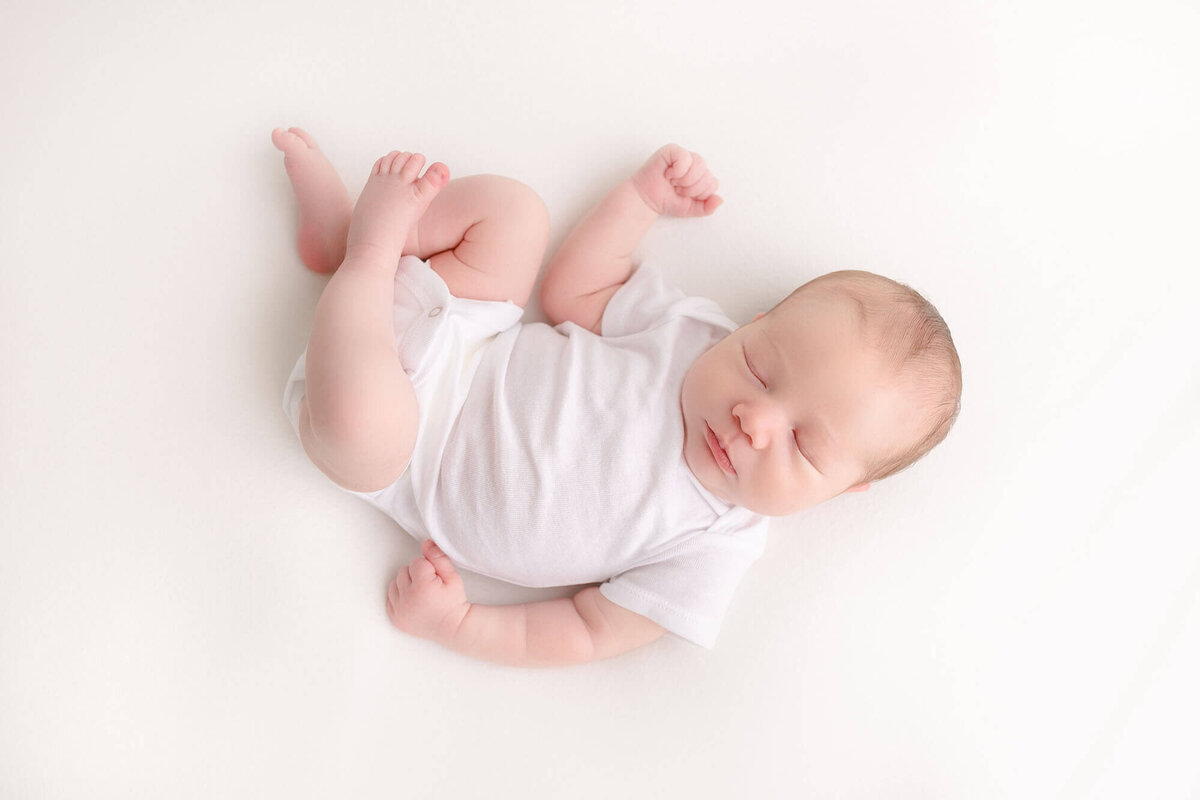 newborn baby in white onesie laying on a white backdrop