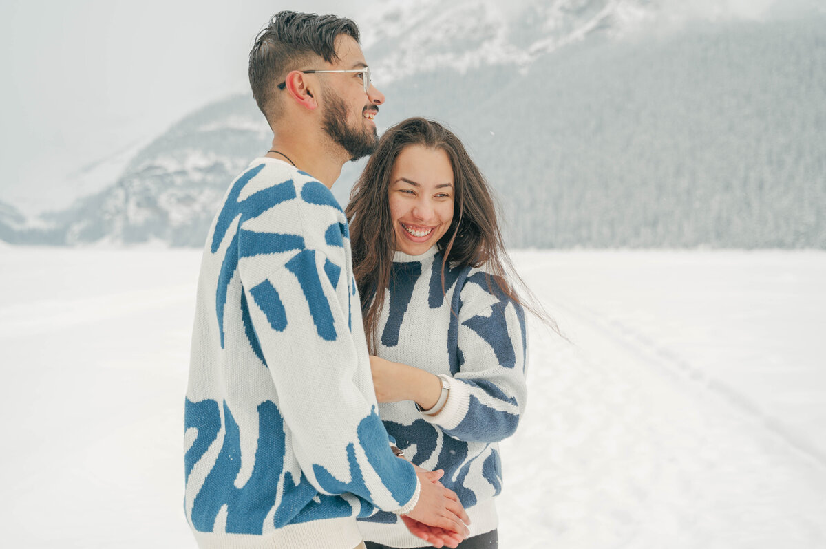 Couple in cozy sweaters holding hands in snowy Banff landscape.