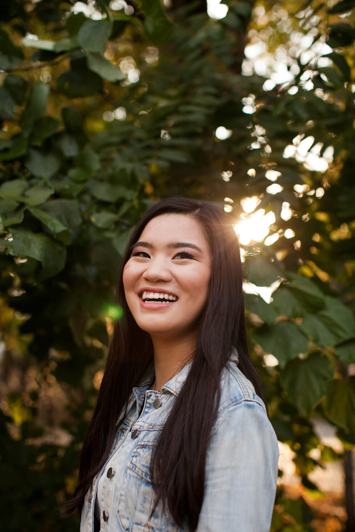A lovely Asian American teen girl laughs in the backlit sun for her senior portraits. Captured by Springfield, MO senior photographer Dynae Levingston.