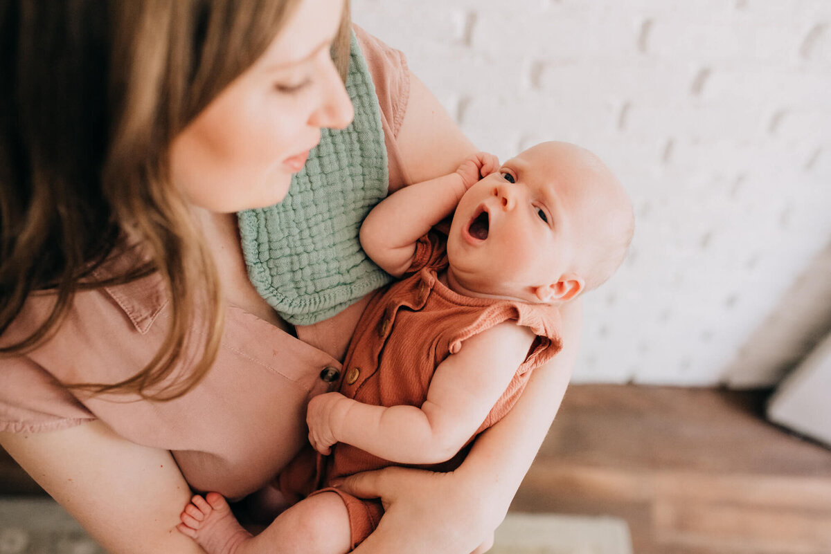 A baby yawns while her mother holds her in front of a bright white wall