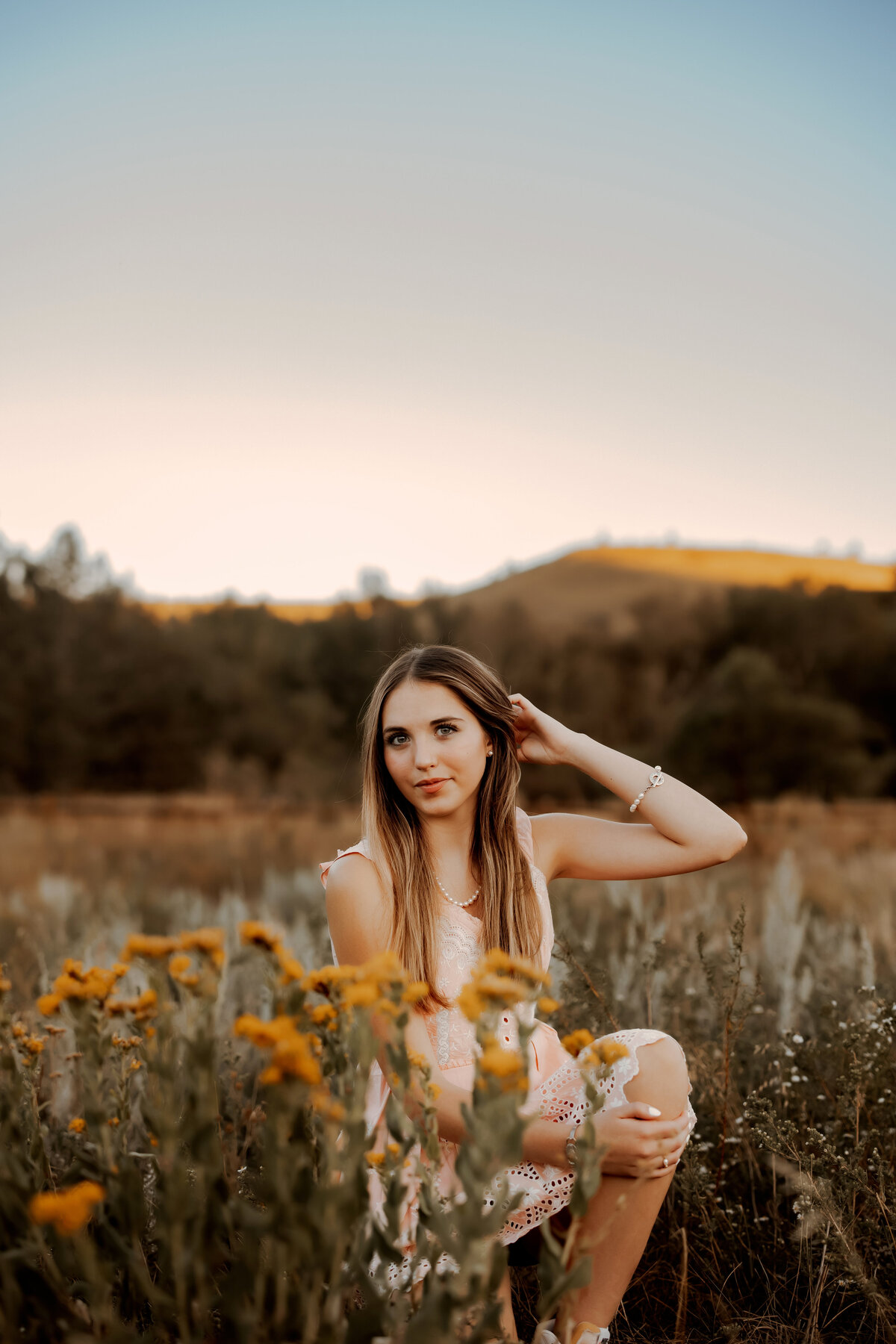 Senior girl in peach dress kneeling in front of yellow flowers in Boulder, Colorado