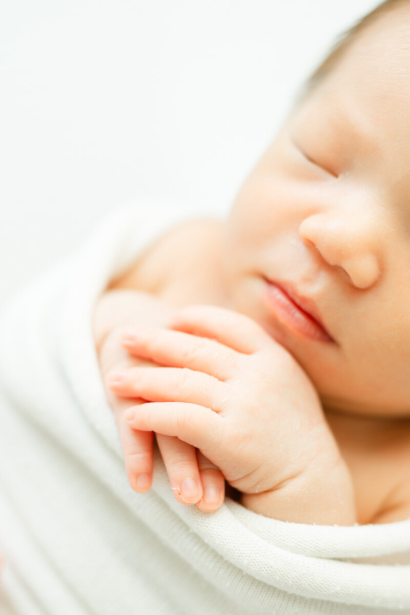 macro newborn portrait of an infant's hands. Her nose and mouth can also be seen in the background of this close-up picture captured by a newborn photographer in Austin, TX.