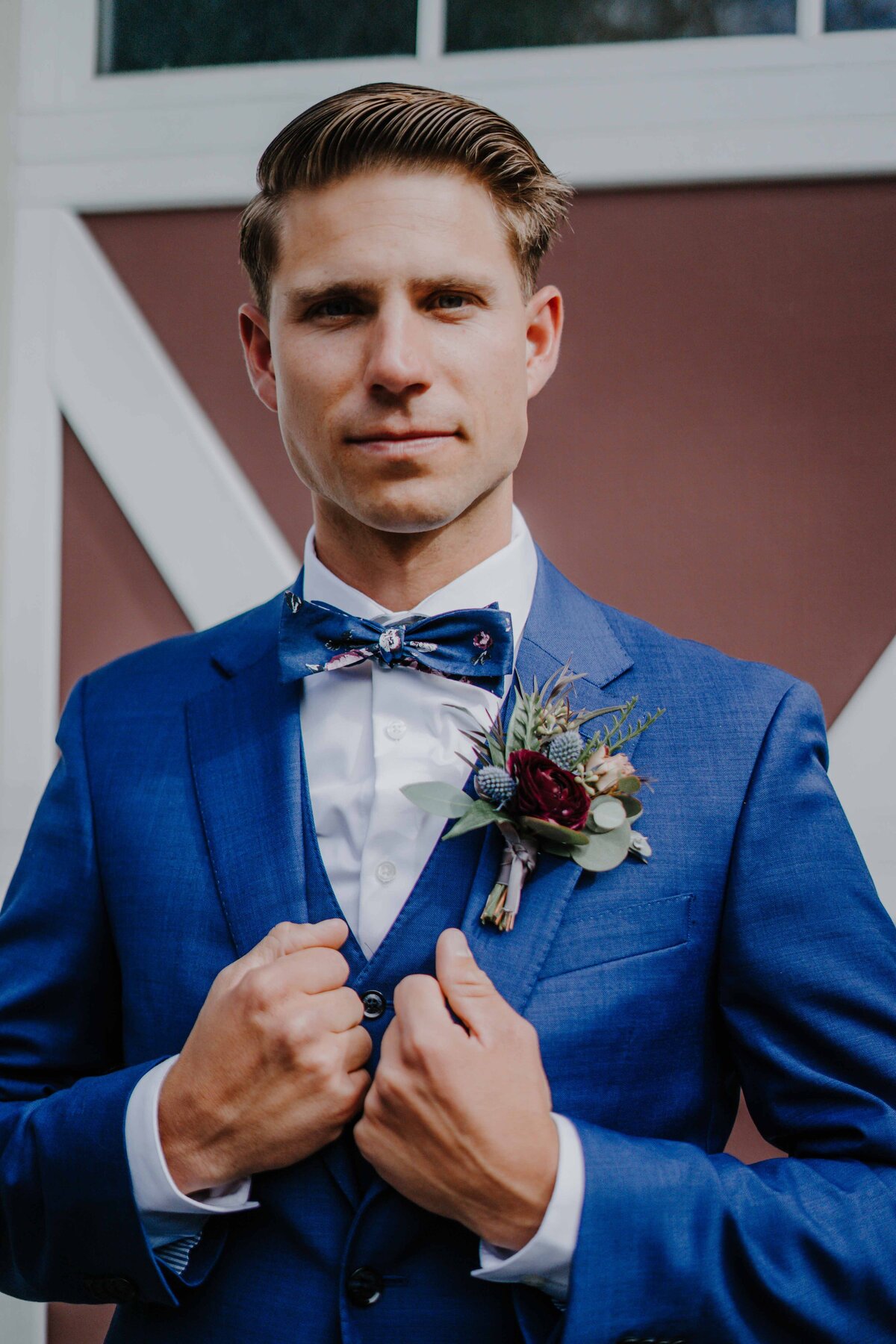 groomsmen in a blue suit posing in front of a red barn