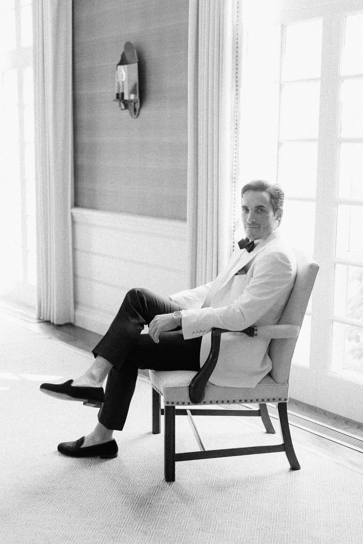 A black and white photo of the groom sitting in a chair at the Shoresacres CC. 