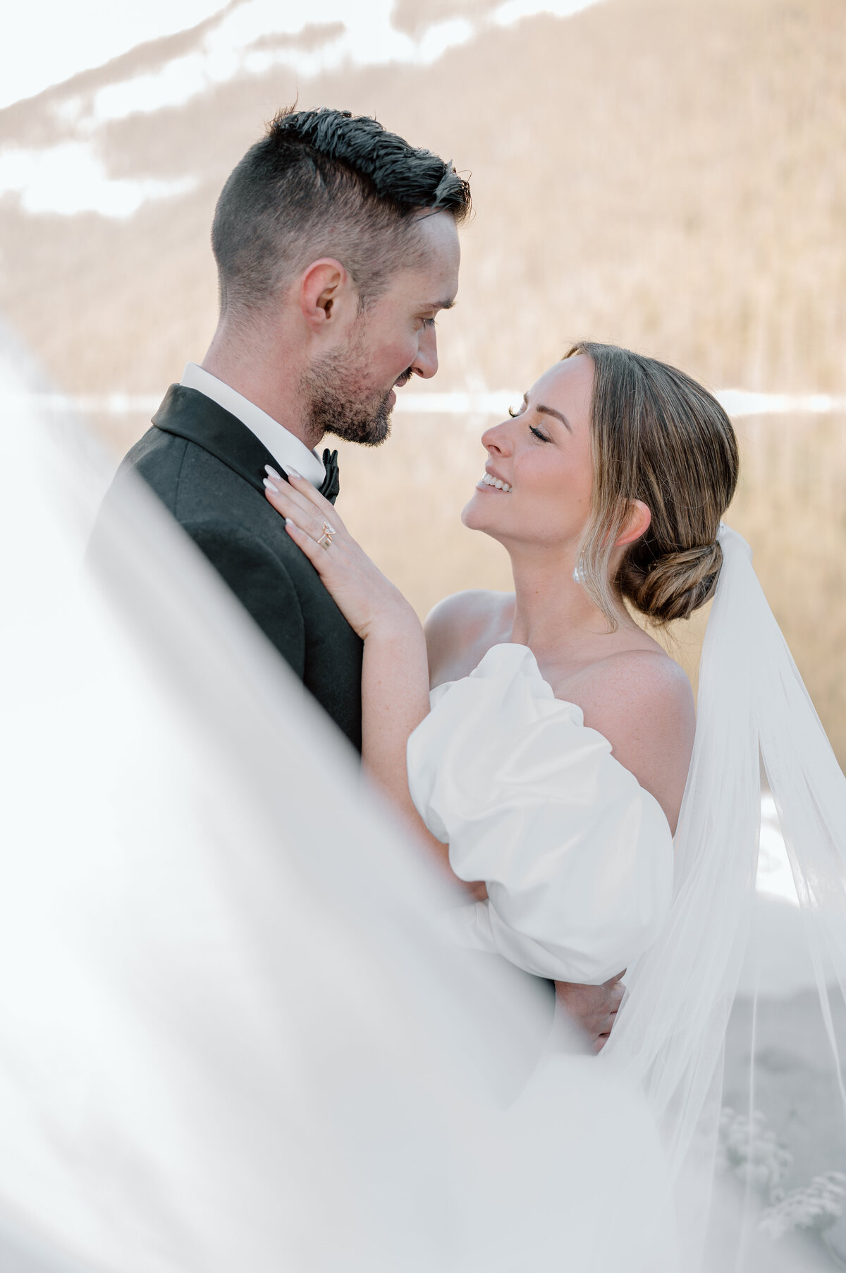 Newlyweds smiling at each other in front of forested mountain backdrop