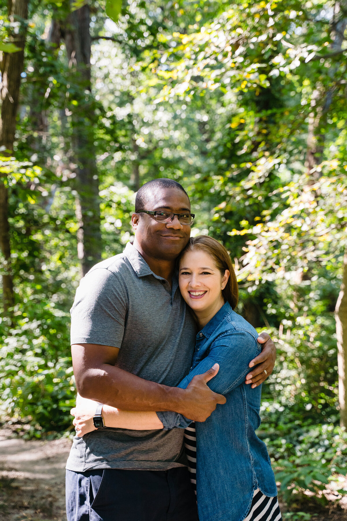 A couple hugging and standing in a small wooded area.