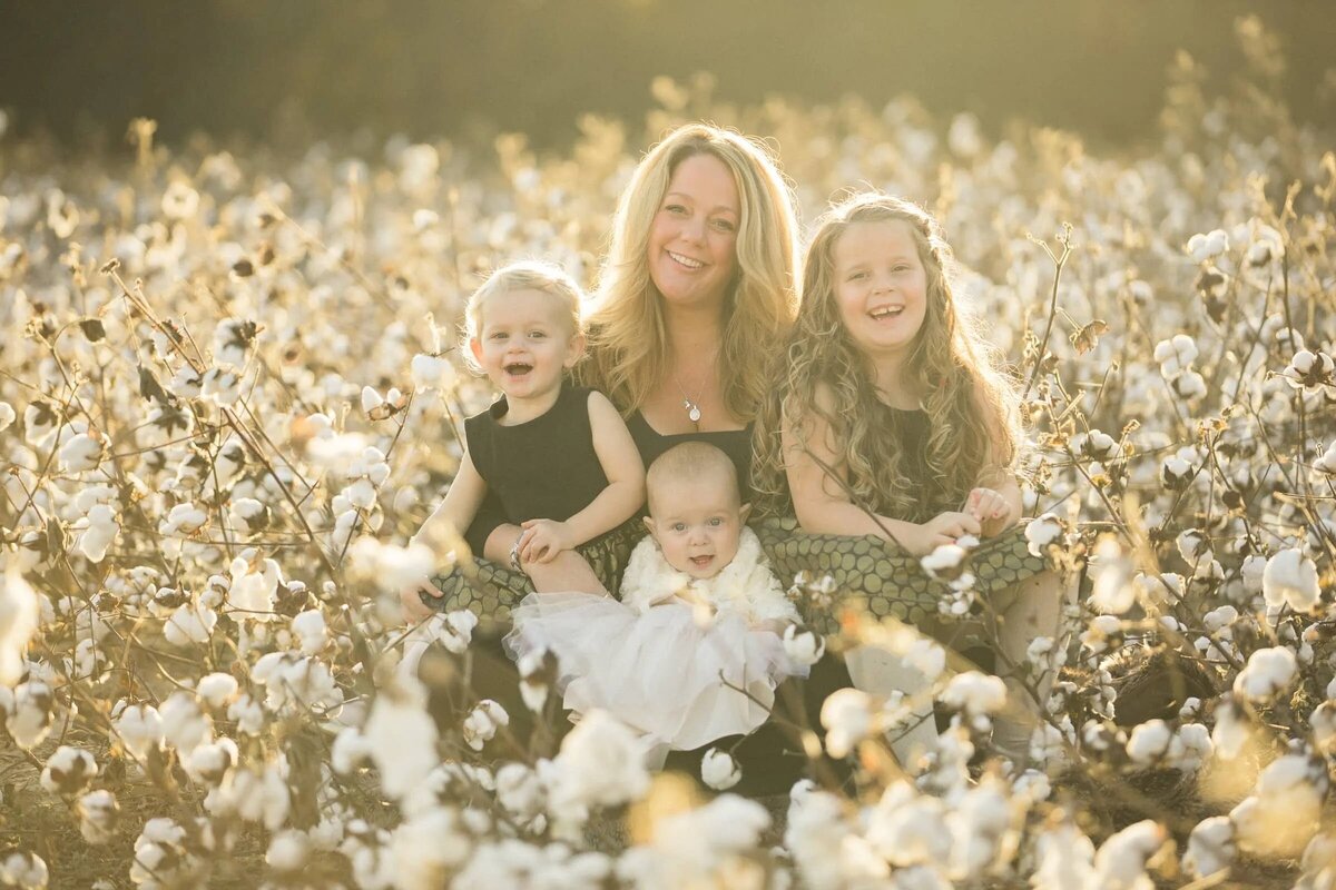 A mom sitting in a field of flowers with three small kids.
