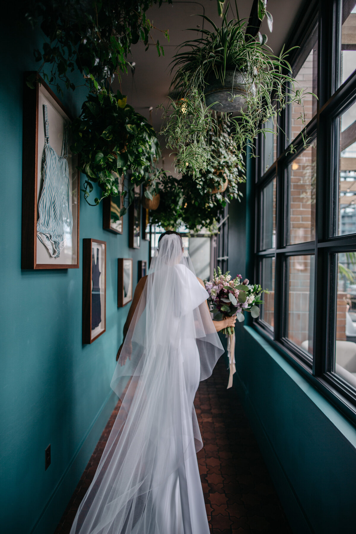 Bride walking down hallway decorated with hanging plants in route to first look