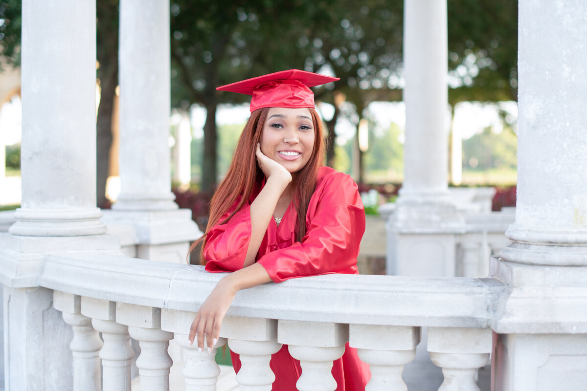 High school senior girl in cap and gown leaning against stone railing.
