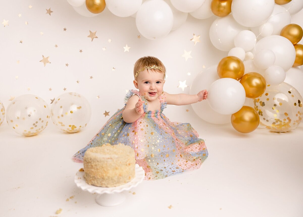 baby girl pointing to balloons with cake in front of her for pictures in portland