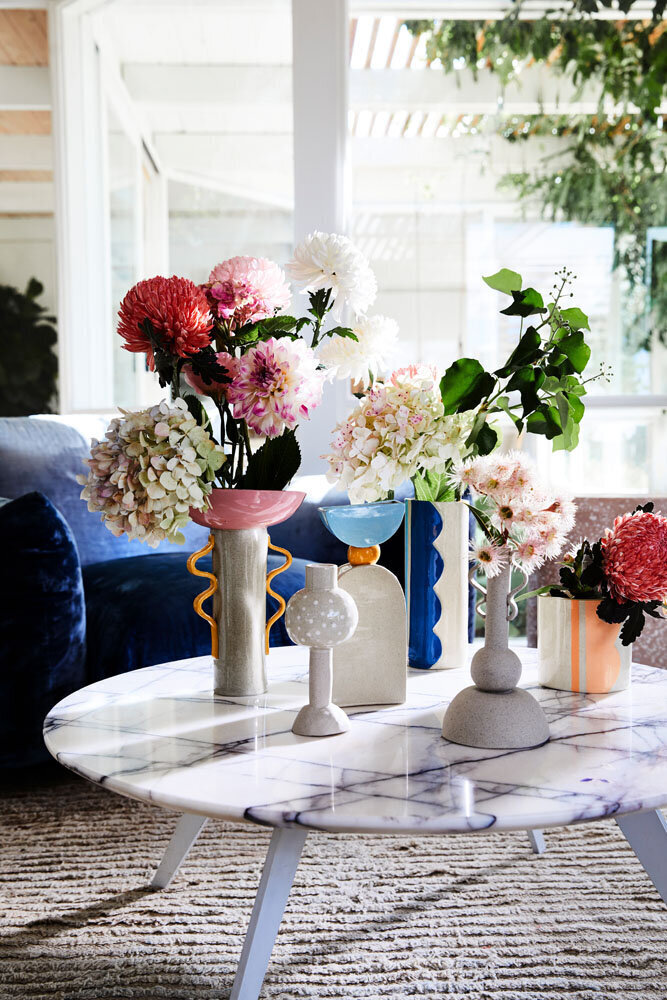 Artfully styled marble coffee table with vases and seasonal florals in a sunlit lounge room.