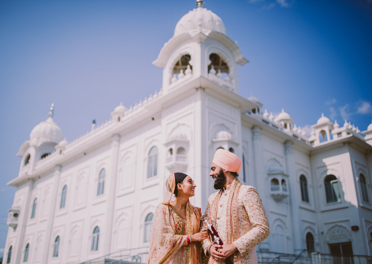 Sikh amritdhari bride and groom look at each other with the temple behind them in brampton at dashmesh darbar gurudwara